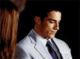 a man in a suit and tie looks down at something while a woman stands behind him