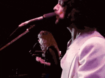 a man singing into a microphone while a woman plays a guitar in the background