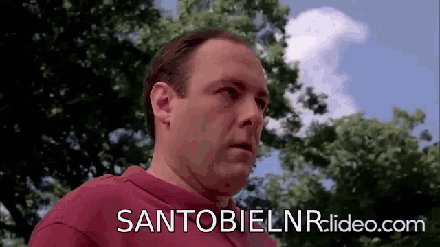 a man in a red shirt with the website santo bielnr.video.com in the background