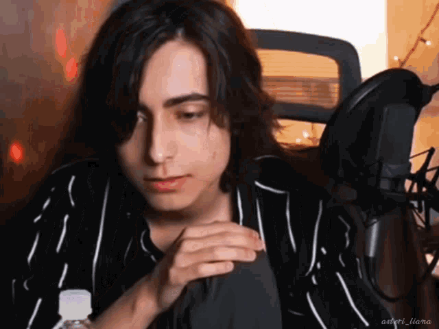a young man with long hair is sitting in front of a microphone with a bottle of water in front of him