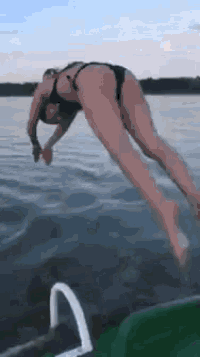 a woman in a bikini is jumping into a lake from a boat .