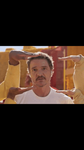 a man with a mustache is surrounded by people making a circle with their hands around his head .