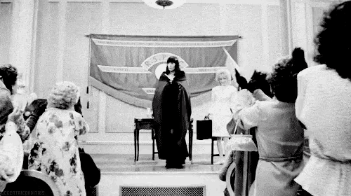 a woman in a purple cape is standing in front of a group of people .