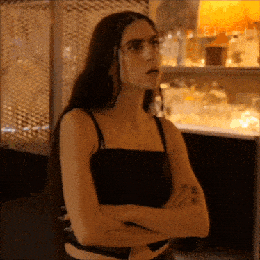 a woman in a black tank top is standing with her arms crossed ..