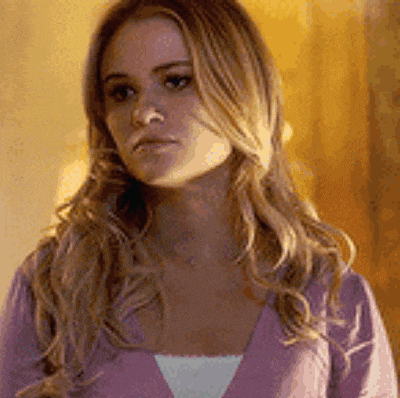 a woman with long blonde hair is wearing a purple sweater and looking at the camera .