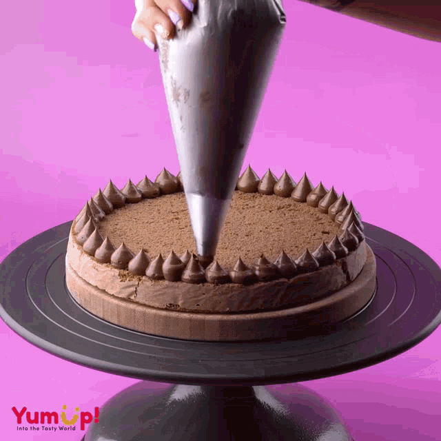 a chocolate cake is being decorated by a person with a yum up logo in the background