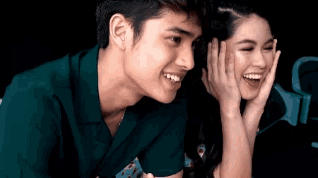 a man and a woman are laughing together and the man is covering his face with his hand