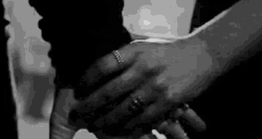 a man and a woman are holding hands in a black and white photo . the woman is wearing a wedding ring .