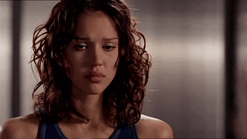 a woman with curly hair and a blue tank top is looking down .