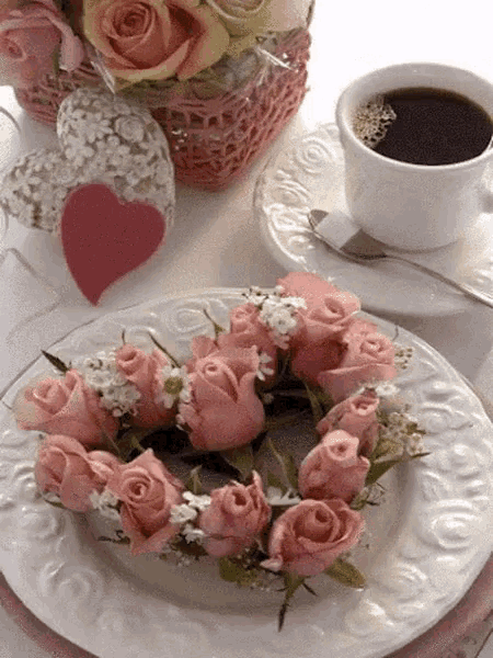 a wreath of pink roses is on a white plate next to a cup of coffee