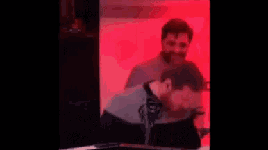 two men are sitting in front of a microphone in a room with a red background .