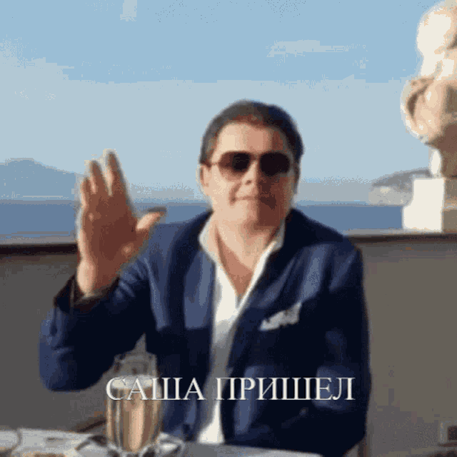 a man wearing sunglasses and a blue jacket is sitting at a table with a glass of wine