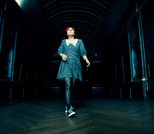 a woman in a blue dress and black polka dot tights stands in a dark hallway