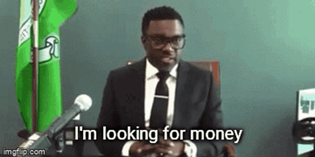 a man in a suit and tie is sitting in front of a microphone and saying `` i 'm looking for money ''
