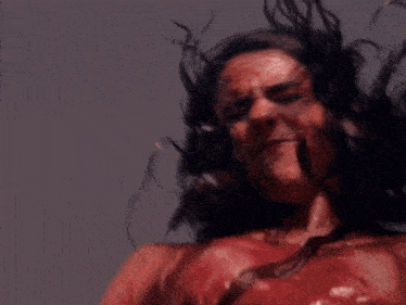 a woman with long hair and red paint on her face is dancing with her hands in the air .