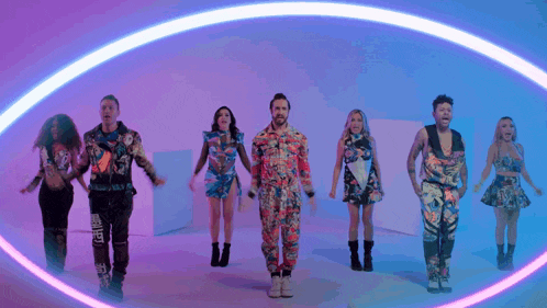 a group of people are dancing in a circle with a neon light behind them