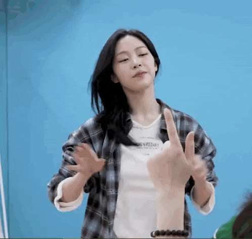 a woman wearing a plaid shirt and a white shirt is giving a peace sign .