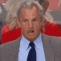 a man in a suit and tie is making a funny face while sitting in front of a group of people .