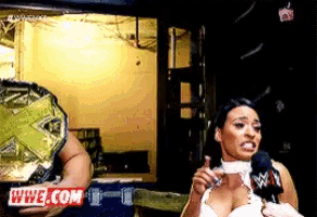 a woman is talking into a microphone while a man holds a wwe championship belt