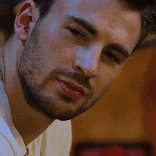 a close up of a man 's face with a beard wearing a white shirt .