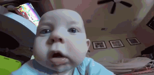 a baby is making a funny face in a living room with a ceiling fan .