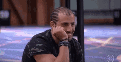 a man with a braided head is sitting with his hand on his chin .