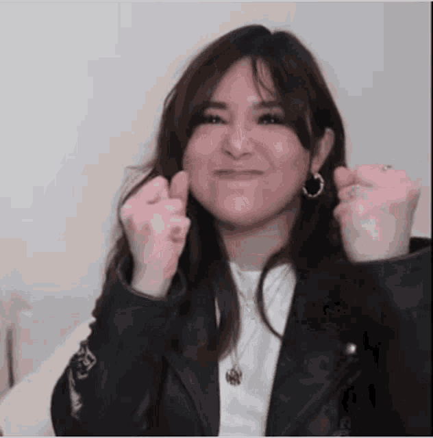 a woman wearing a leather jacket and earrings is making a funny face with her hands .