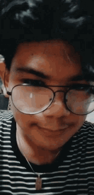 a young man wearing glasses and a striped shirt smiles for the camera