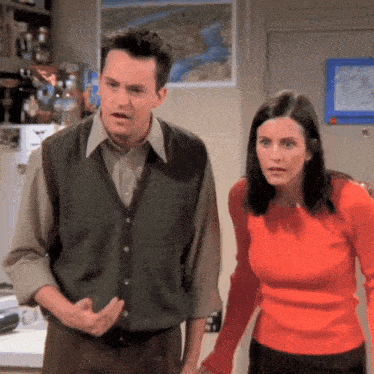 a man in a vest and a woman in a red shirt are standing next to each other