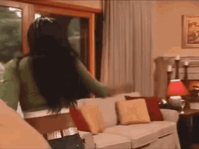 a woman is standing in a living room next to a couch and a window .