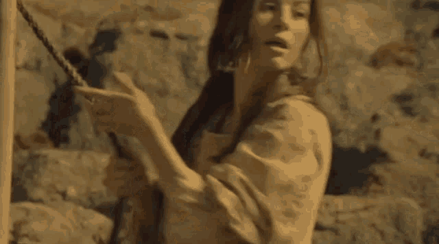 a woman with long red hair is sitting on a rock in the desert looking at the camera .