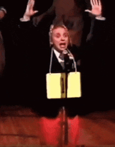 a man in a suit and tie is holding a microphone and a yellow sign that says 1 on it