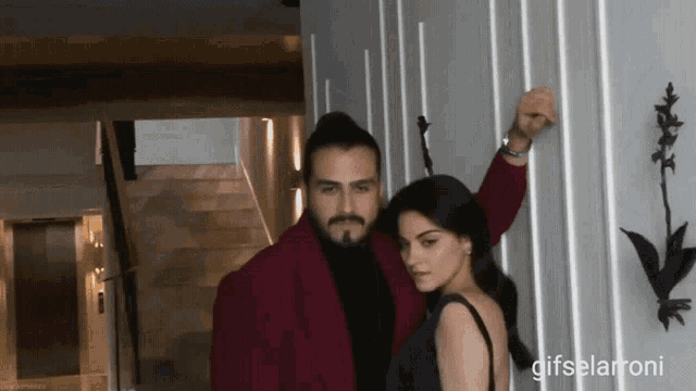 a man in a red jacket leans against a wall with a woman in a black dress