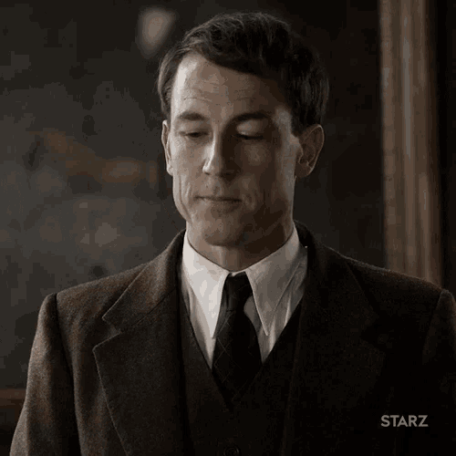 a man wearing a suit and tie is standing in front of a starz logo