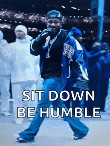 a man in a blue jacket holds a microphone with the words sit down be humble above him