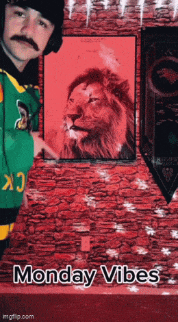 a man with a mustache is standing in front of a painting of a lion with monday vibes written on the bottom