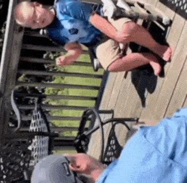 a man is holding a child in his arms while sitting on a deck .