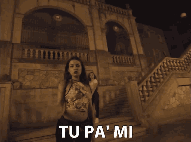 a woman in a floral top is standing in front of a building with the words tu pa ' mi written below her
