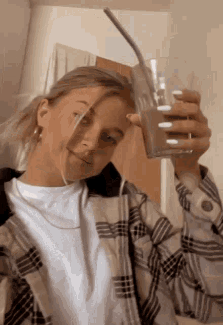 a woman in a plaid shirt is holding a glass with a straw in her hand