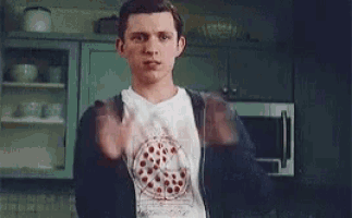 a man is standing in a kitchen wearing a pizza shirt and giving the middle finger .