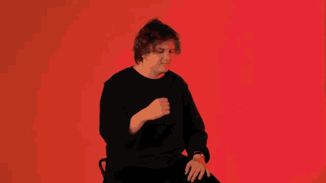 a man in a black shirt sitting in front of a red wall