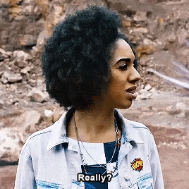 a woman with an afro is talking to someone while wearing a denim jacket and a necklace .