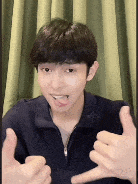 a young man is sticking his tongue out and giving a thumbs up sign