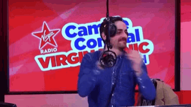 a man stands in front of a microphone in front of a virgin radio sign
