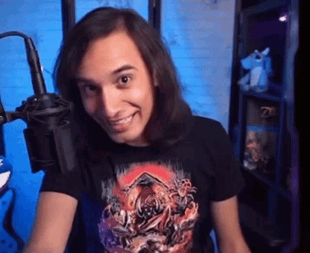 a man with long hair is smiling in front of a microphone in a room .