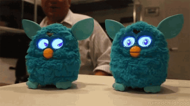 two blue furby toys are sitting on a table with a man behind them