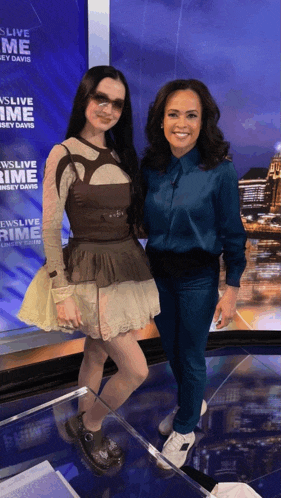two women are posing for a photo in front of a sign that says ' ewslive prime '