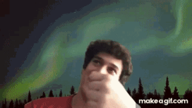 a man in a red shirt is making a funny face in front of the aurora borealis