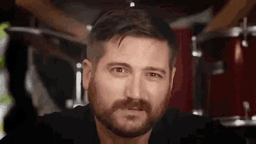 a man with a beard and mustache is standing in front of a drum set .