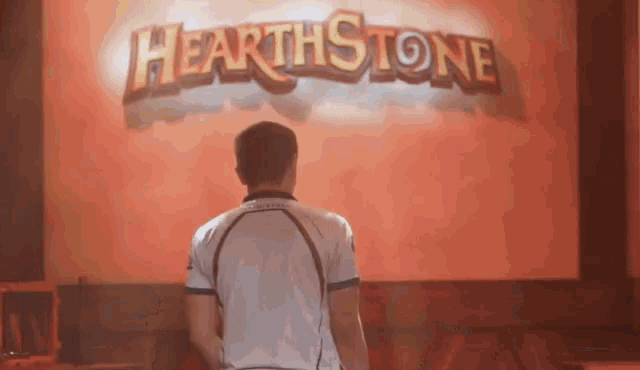 a man in a white shirt stands in front of a hearthstone sign